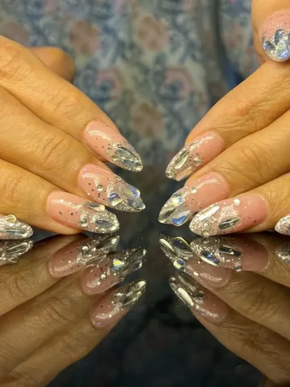 A dramatic set of long stiletto nails with a sheer pink base and accent nails covered in large, sparkling silver rhinestones.