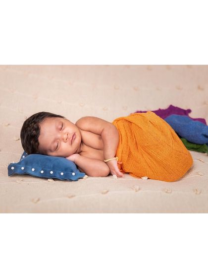 A peaceful portrait of a newborn sleeping on a small blue pillow. The colorful wraps trailing behind add a touch of artistry to this simple and classic shot.