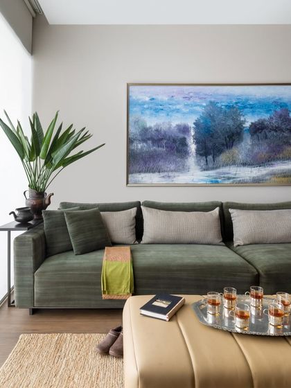 A close-up of the family lounge seating, showing the soft texture of the sofa fabric and the warm tones of the leather ottoman. A large plant and a beautiful painting add life and colour to this inviting space.