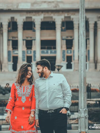 A classic, romantic shot of a couple walking in front of a grand, colonial-style building, perfect for a timeless pre-wedding album.