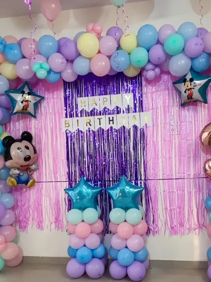 A pastel Mickey Mouse themed decoration for a third birthday. This design uses a soft color palette of purple, pink, and blue for the balloon arch, accented with a pink shimmer backdrop and Mickey Mouse foil balloons.