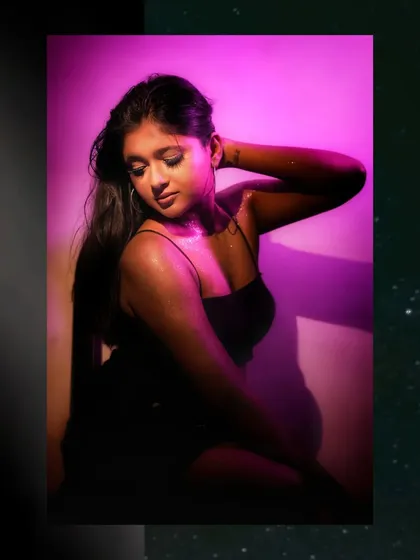A glamorous and glitzy portrait, with the model under a vibrant pink light, looking down gracefully.