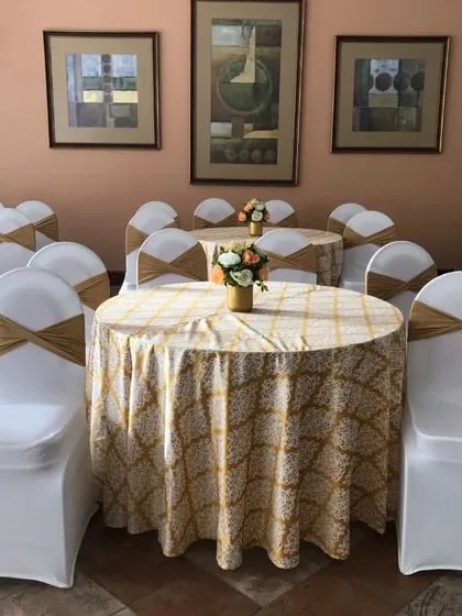 A clean and elegant seating arrangement for guests. We used round tables with patterned cloths, white chair covers with golden sashes, and simple floral centerpieces for a classic look.