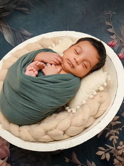 A striking portrait using a dark, moody floral backdrop. The contrast makes the peacefully sleeping baby, swaddled in teal, the clear focus of the image.