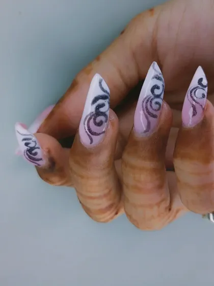 A dramatic set of extra-long stiletto nails with a pink ombre base and black tribal-style swirls.