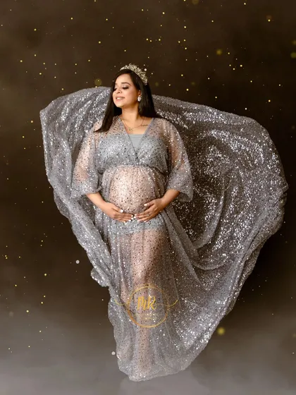 A solo portrait showcasing our sparkling silver maternity gown. The fabric is tossed to create a beautiful, flowing shape, enhanced by a magical bokeh effect.