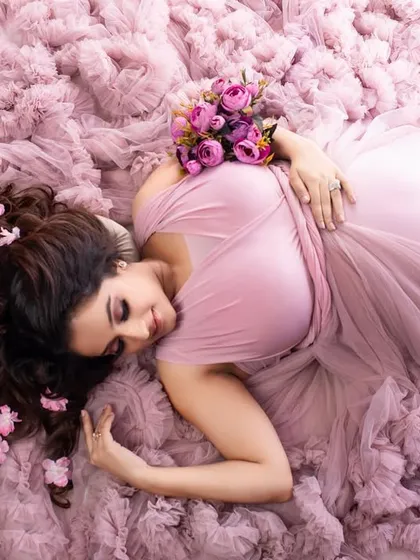 An artistic overhead shot with the client lying on a bed of soft pink ruffles. The flowers in her hair and the gentle pose create a dreamy and romantic 'sea of petals' effect.