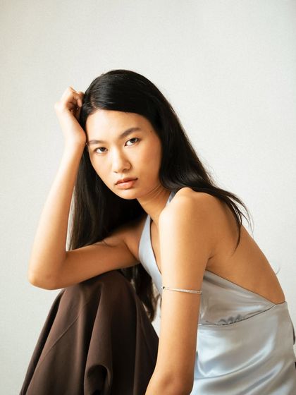 A seated portrait with a focus on a relaxed yet direct expression. The soft, natural-style lighting and simple composition make this a strong, compelling image for a fashion lookbook.