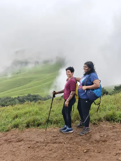 Two women enjoying the stunning view from a ridge on the Nethravathi trail. The rolling green hills disappearing into the clouds is a signature landscape of this Western Ghats trek.