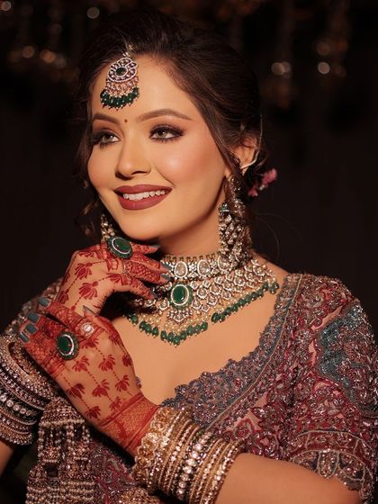 A close-up of a bride's reception look, with her emerald jewelry and her beautifully stained mehandi hands.