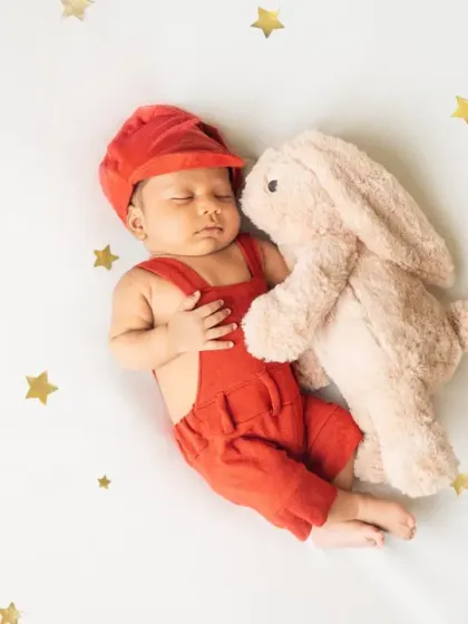 Dressed in a cute red outfit and snuggled up with a soft bunny, this newborn is ready for a nap under a sky of golden stars.