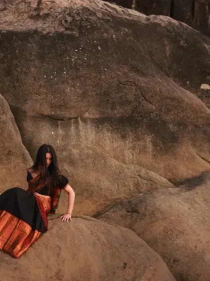 A wide, dramatic shot of the model amidst large rock formations, creating a powerful and artistic composition.