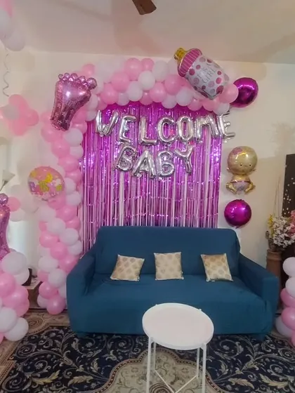 A pink and white "Welcome Baby" decoration with a foil curtain backdrop and balloon pillars.
