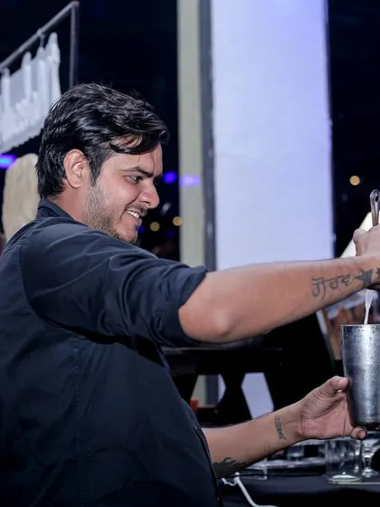 One of my skilled mixologists pouring a freshly shaken cocktail. The tattoo on his arm, 'Maa', adds a personal touch, reflecting the heart my team puts into their work.