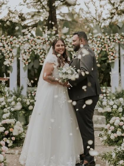 A magical moment as a couple is showered with petals after their Christian wedding ceremony. The backdrop of white flowers and greenery creates a fairytale setting.
