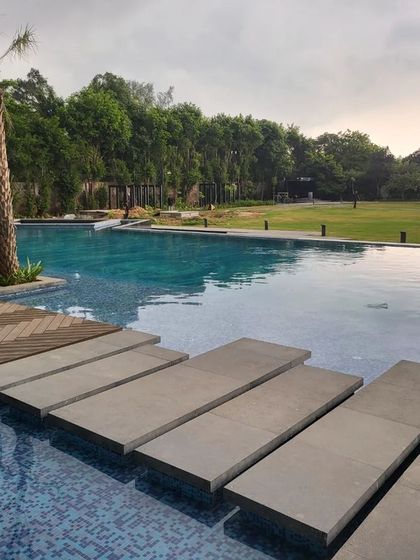 Floating stone steps provide a stylish path across the corner of a large swimming pool. This feature is both functional and highly aesthetic, enhancing the modern design of the farmhouse landscape.