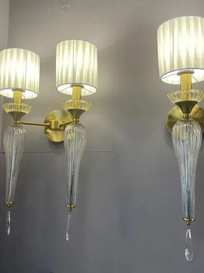 This pair of wall lights combines several classic elements: pleated fabric shades, ribbed glass bodies, and delicate crystal drops. The design is intricate and luxurious, perfect for adding a layer of texture and refinement.