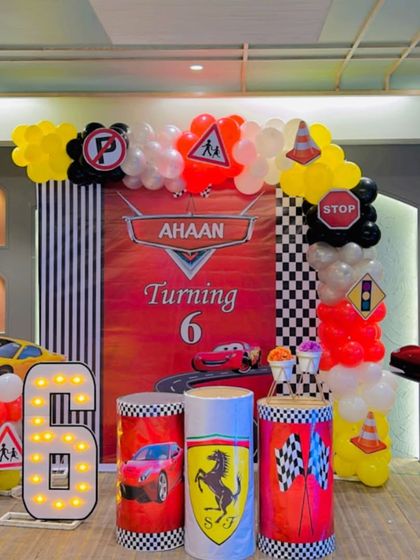 A Lightning McQueen car-themed party for a 6th birthday. This setup features a custom backdrop, Ferrari-themed plinths, traffic sign props, and a large marquee number '6'.