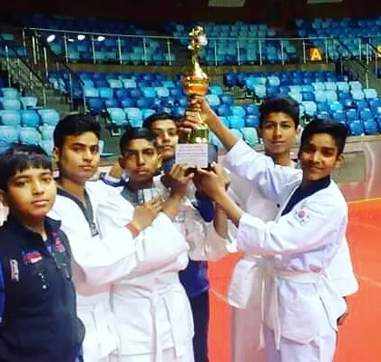 The pride of victory. Our team of young champions holding up their trophy after a national karate championship. We train students to compete, test their skills, and represent our dojo with honor and sportsmanship.