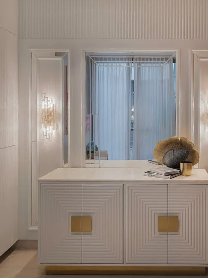 Another angle of the white and gold credenza, showing how it interacts with the wall sconces and mirror behind it. The top provides a perfect surface for displaying curated decor objects.