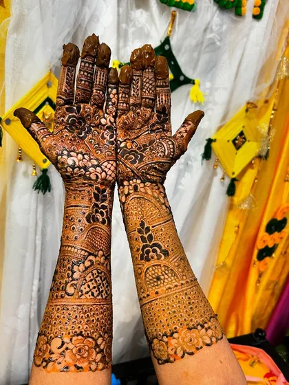 This full bridal mehendi was done against a festive yellow backdrop, highlighting the fresh henna paste. The design includes detailed finger work and thick bands on the forearm.