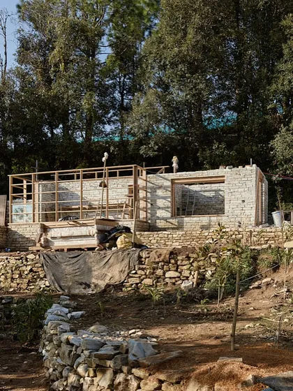 The timber frame of a building rises from its stone foundation. This combination of materials is a hallmark of our Himalayan projects, providing both structural stability and a warm, inviting interior.
