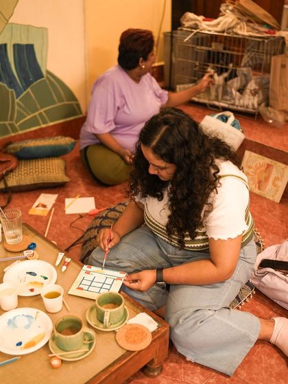 A participant focuses on her painting while a volunteer tends to the kittens in their carrier nearby.