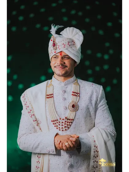 A close-up portrait of the groom in his white sherwani and turban, highlighting his wedding day glow.