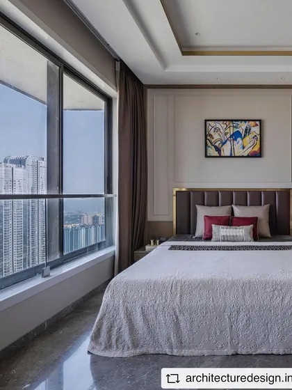 This bedroom in the 'Aria Residence' offers stunning views of the Mumbai skyline. The design is kept elegant and understated, with a neutral color palette and a striking piece of abstract art.