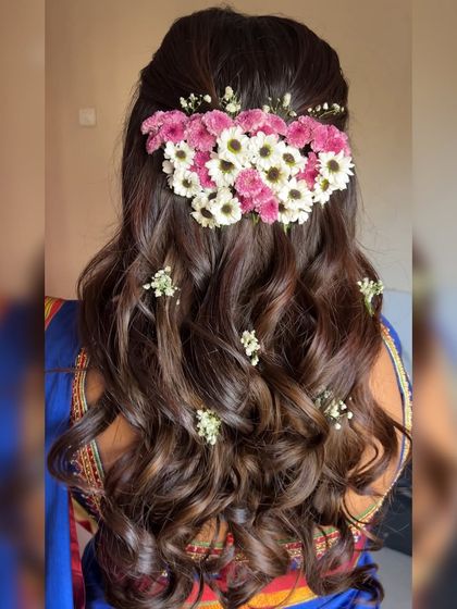 A detailed look at the beautiful floral hairstyle created for this guest. The soft curls are gathered and adorned with fresh pink and white flowers, adding a touch of natural elegance that perfectly matches her traditional attire.