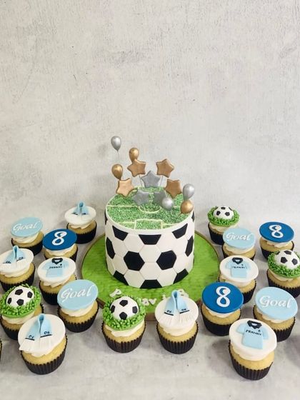 A football-themed cake and cupcake set. The cake looks like a football, and the cupcakes are decorated with jerseys and soccer balls.
