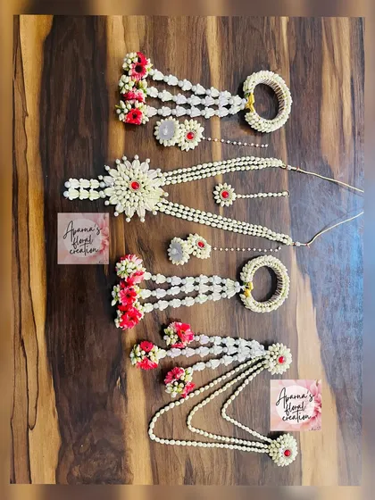 A collection of baby shower jewellery pieces made with white jasmine buds and red accent flowers. The image shows two different styles of hath phool and a matching necklace set.