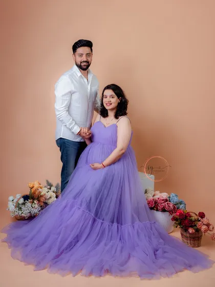 A lovely seated portrait from a studio maternity session. The flowing purple gown creates a beautiful shape, and the floral props add a touch of color and elegance to the scene.
