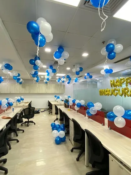 A full office space decorated for an inauguration ceremony, with blue and white balloon bunches and a "Happy Inauguration" foil banner.