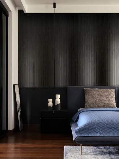 A close-up of the bedroom in Villa Aish, where a fluted black feature wall adds texture and depth. The design focuses on a minimalist yet warm aesthetic, using a combination of rich wood flooring, dark tones, and soft lighting to create a restful sanctuary.