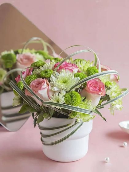 A chic and modern floral arrangement with pink roses and green chrysanthemums, creatively designed in a white pot.