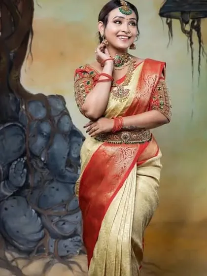 A classic bridal portrait. The model wears a traditional cream and red silk saree, with makeup that emphasizes her eyes and a simple red bindi to complete the look.