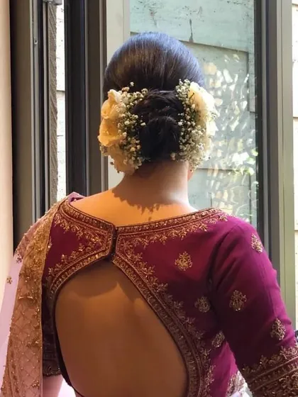 A back view of a beautiful braided bun, adorned with white roses and baby's breath. The combination of textures makes this a visually interesting and elegant updo.