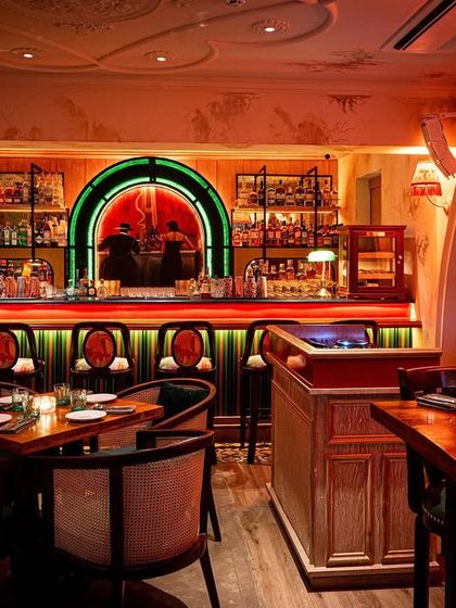 The bar area at Los Cavos, glowing with red and green neon. The design uses lighting to shift the mood from an intimate restaurant to a high-energy bar, showcasing the space's versatility.