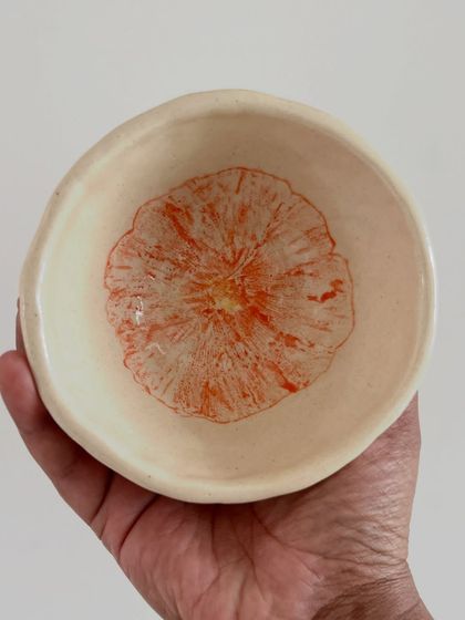 A small, delicate bowl with a marigold flower print inside. This technique uses a real flower to transfer the pattern onto the clay.