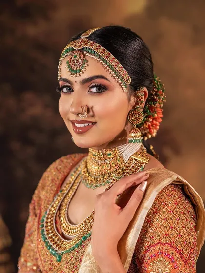 A stunning South Indian bridal look featuring a blouse with heavy, multi-colored embroidery. The intricate patterns and rich jewel tones of the threadwork are designed to complement the grand temple jewelry.