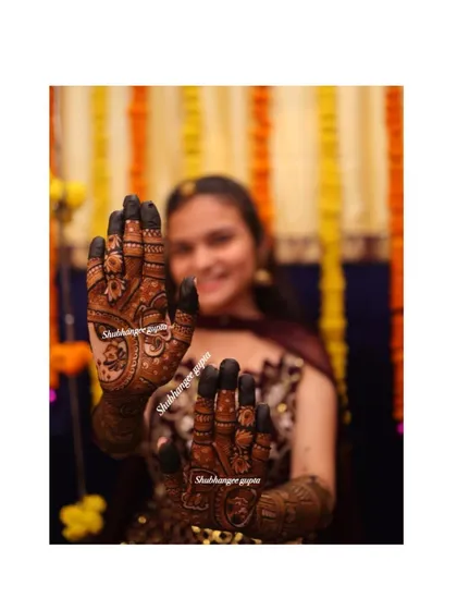 A happy bride showing off her beautiful mehndi. The design features portraits and traditional symbols, making it a perfect reflection of her joy.
