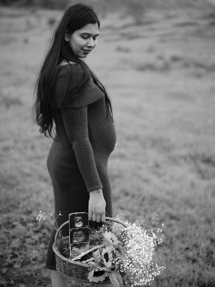 A serene black and white portrait of the mom-to-be in a field, holding a basket of flowers and sonogram pictures. Her gentle expression is full of quiet joy.
