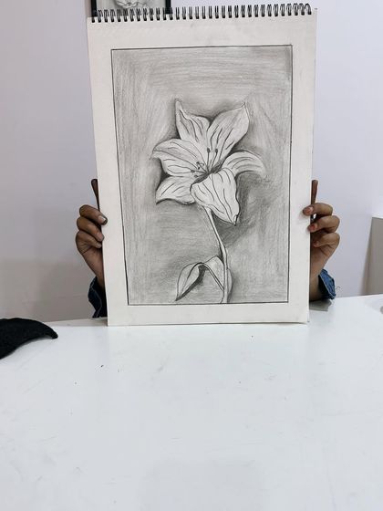 A student holds up their amazing flower sketch. The contrast between the light petals and dark background is so effective.