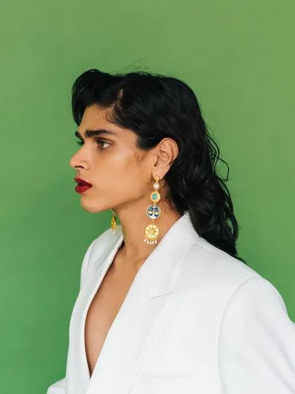 A profile shot for an Amama Jewels campaign. This image highlights the length and detail of the statement earrings against a bold red lip and white blazer.