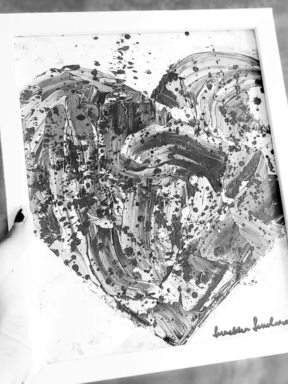 Holding the framed black and white heart. The simple white frame makes the monochrome artwork stand out. It’s a contemporary piece that fits well in a modern, minimalist space.