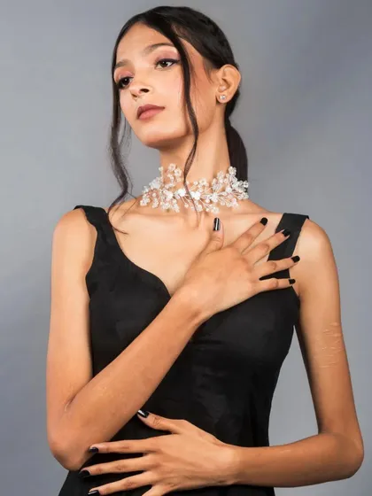 A classic portrait pose that highlights the model's features, the crystal choker, and the elegant simplicity of the black dress. The neutral grey background ensures the subject remains the sole focus.
