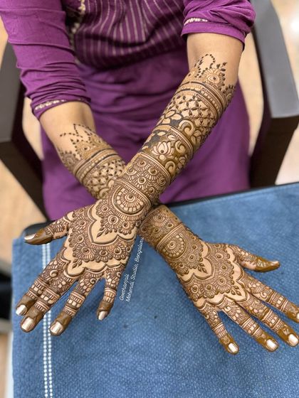 A crossed-arm pose showing the full effect of this intricate bridal mehendi, with patterns that wrap beautifully around the arms.