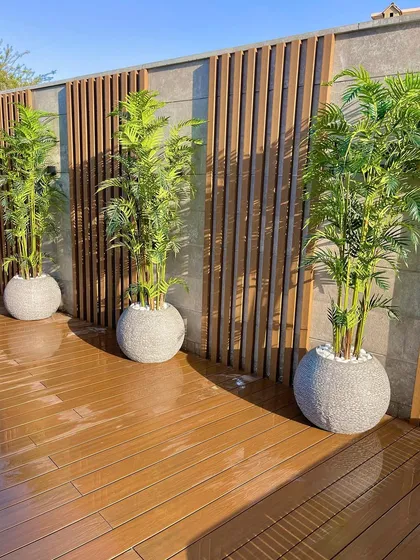 A clean and modern patio design with a wooden deck and a feature wall with vertical wood slats. We use large, simple planters with identical plants to create a sense of rhythm and order.