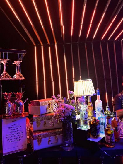A stylish corner of our neon bar setup, featuring vintage-style suitcases, pineapple decor, and a backdrop of glowing orange LED light strips that create a warm, energetic ambiance.